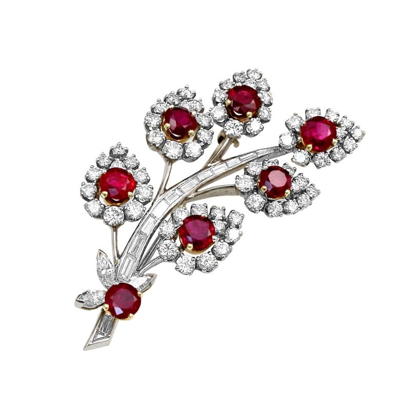 A beautiful flower motif pin prong-set with seven round, brilliant-cut burmese ruby accented with round brilliant-cut diamonds. Stamped McT, Platinum.