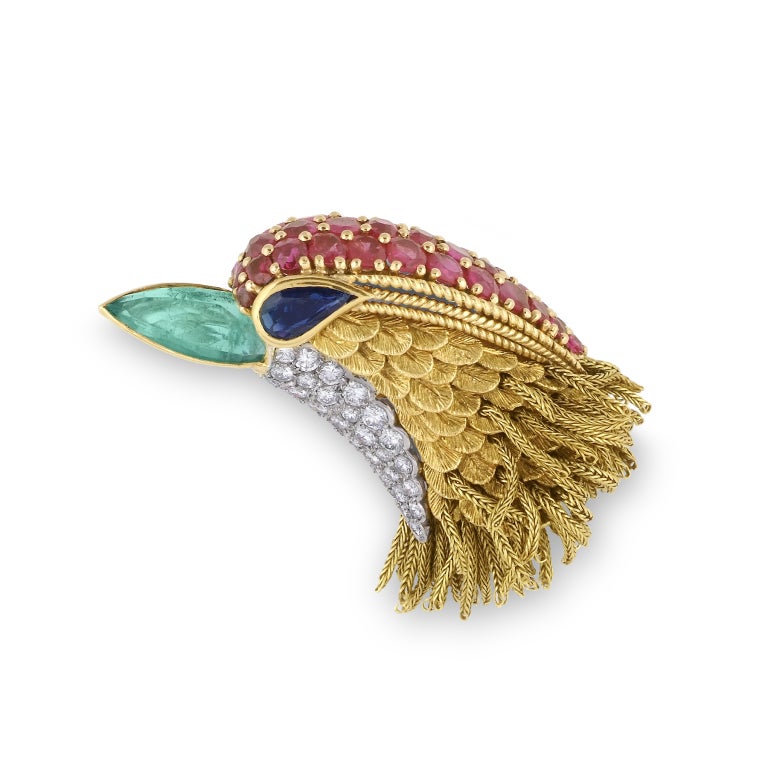 Designed as a stylised bird's head, to an articulated yellow gold fringe, the head composed of textured gold feathers, the throat embellished with pavé-set brilliant-cut diamonds, the tapering crest set with circular-cut rubies, the eye composed of