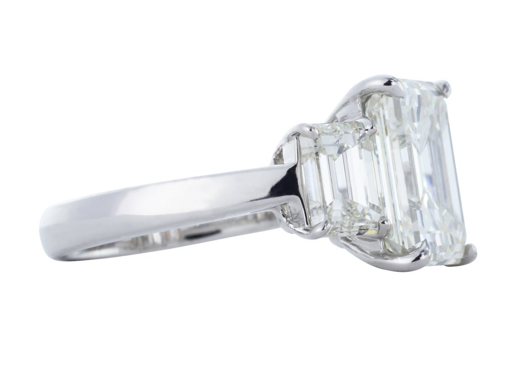 Platinum three stone style engagement ring consisting of 1 emerald cut diamond, measuring 10.85 x 9.08 x 5.72 mm, weighing 5.05 carats, having a color and clarity of J/VVS2 and GIA report 5141892724. The center stone is flanked by 2 emerald cut