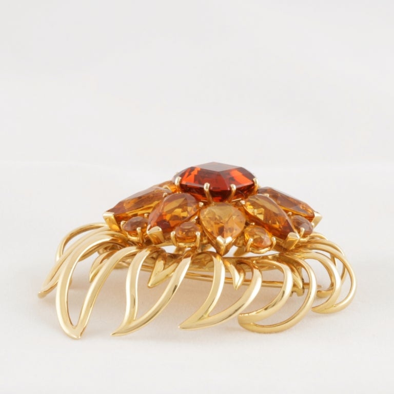 An English, Mid 20th Century 18 karat gold brooch with citrines. The brooch has 8 pear-cut citrines with an approximate total weight of 20.00 carats, 8 round-cut citrines with an approximate total weight of 4.00 carats, and 1 round-cut center