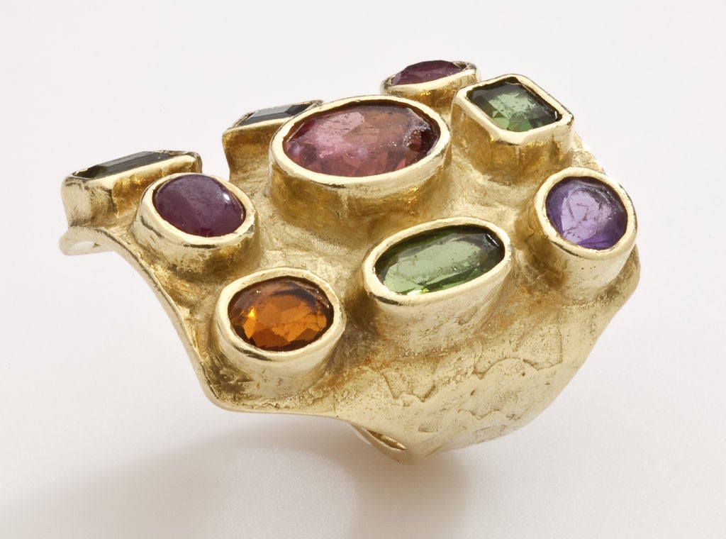 A gold ring by modernist jeweler, Ed Wiener (1918 1991).  In the textured 18 karat gold, Wiener has placed a variety of gem stones, green and pink tourmalines, a sapphire, a ruby, a topaz and an amethyst, giving the ring a rainbow quality.   Wiener,