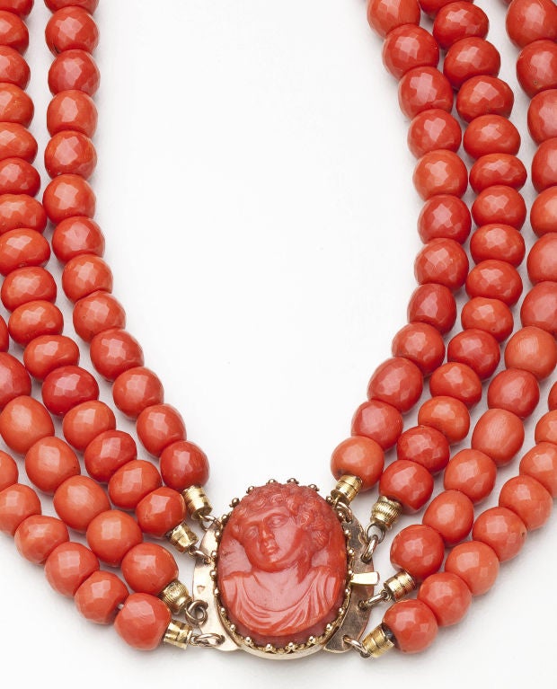 A four strand coral necklace in which approximately 250 beads are faceted and graduating in size from approximatelyh 6.5mm to 10mm.  The necklace is completed by an 18 karat gold clasp with a coral cameo of a young, curly-haired woman. The necklace