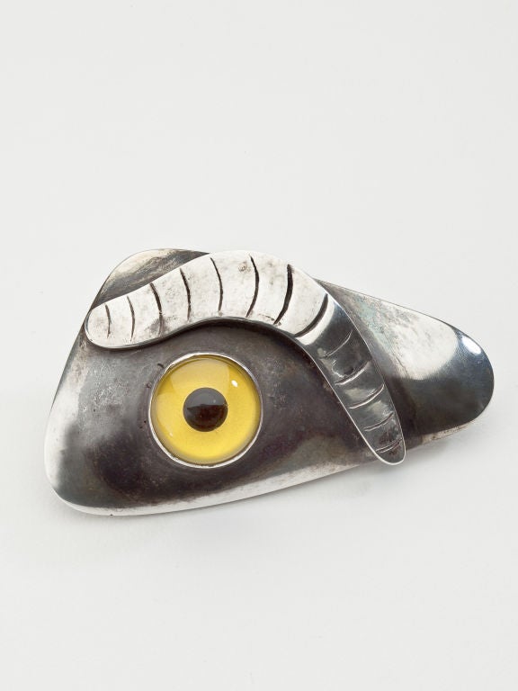A surrealist eye brooch by modernist jewelry designer, Sam Kramer.   Sterling silver with a yellow taxidermy eye.  Signed on the back with Kramer