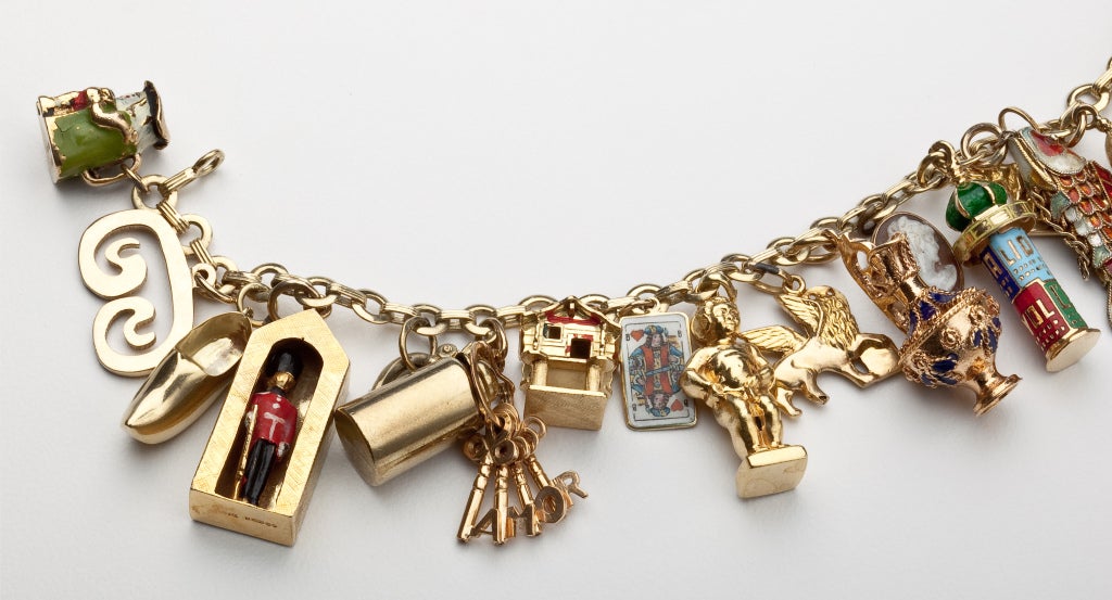 A gold charm bracelet with 22 travel related charms.  Some of the charms have enamel or contain small gem stones.  They include Spanish dancers, the Arc de Triomph in Paris, A Buckingham Palace guard and the keys to Rome.  The charms vary in gold
