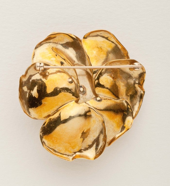 A flower brooch by Cartier in 18 karat gold with diamond accents.  The gold is highlighted by petals with a florentine finish; the 15 diamonds are full cut melee, some of which are en tremblant.  Signed with the Cartier script mark; 18k mark; the