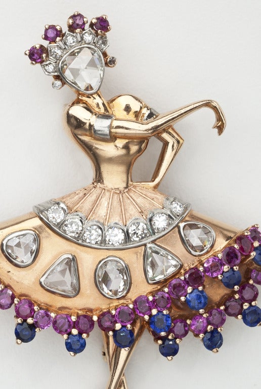A 14 karat gold brooch of a ballerina with diamonds, rubies and sapphires. The gold, which incorporates elements of yellow, pink and white gold, is liberally set with 20 brilliant cut and single cut diamonds, 30 circular cut rubies and 13 circular