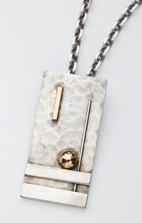 A sterling silver and gold pendant by Art Deco designer, Jean Despres.  The rectangular plaque shows evidence of hand hammering and is highlighted by sterling and 18 karat gold geometric elements.   The pendant is signed 