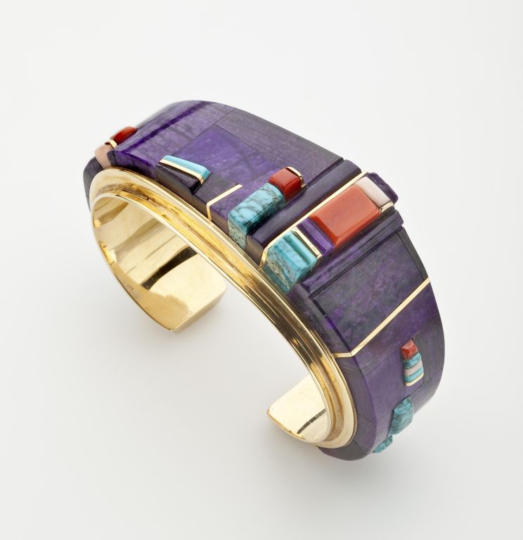 An 18 karat gold cuff bracelet by Charles Loloma inlaid with sugilite, coral and Lone Mountain turquoise. Circa. 1982-85. Matching earrings available. The interior of the bracelet measures 5 1/4