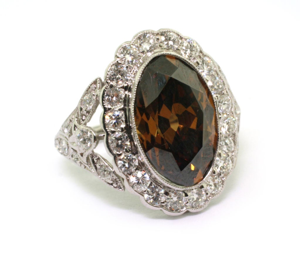 Collet-set to the centre with an oval-shaped fancy dark orangey-brown diamond, within a millegrain border of brilliant-cut diamonds to tapering shoulders of stylised foliate design. Accompanied by GIA Report Number 5111590101 stating that the
