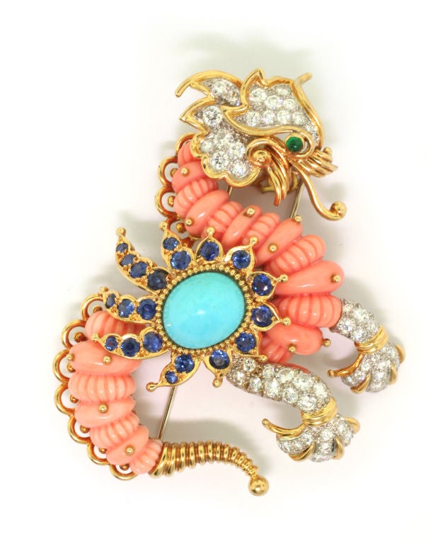 Designed as a stylised dragon, the body composed of fluted coral sections, set to the centre with a turquoise cabochon within a radiating surround of circular-cut sapphires, the feet and head of the dragon embellished with brilliant-cut diamonds and