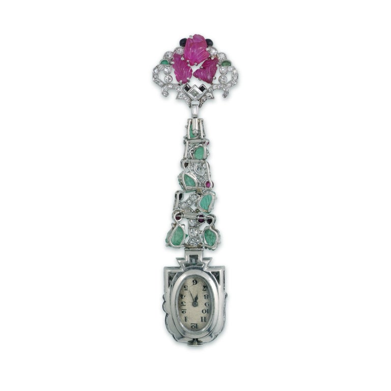 Designed as a carved ruby and circular-cut diamond surmount embellished with onyx and emerald accents, suspending an articulated line of graduated carved emeralds within an openwork diamond-set foliate motif accented with cabochon rubies, to a