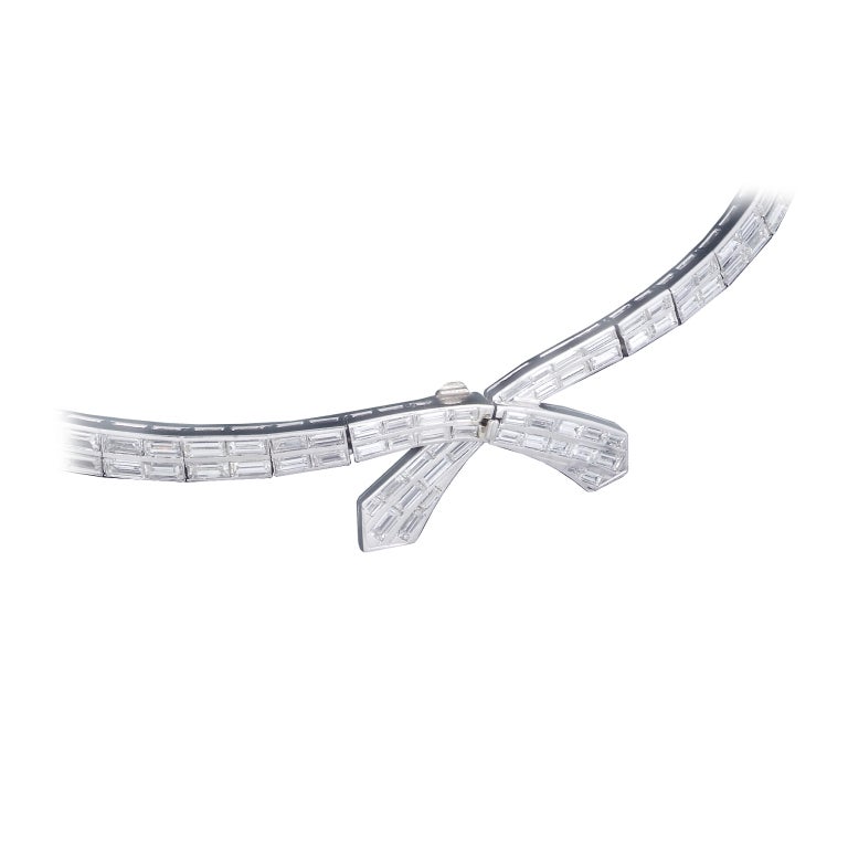 Designed as a solid central stylised bow motif channel-set with baguette diamonds, entwined around two rows of graduated brilliant-cut diamonds, to a smaller bow motif mirrored at the clasp, circa 1960, unsigned, French assay marks for platinum. 