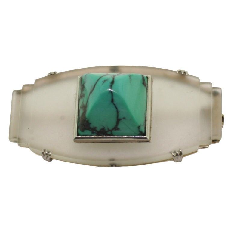 Of geometric design, the central barrel-shaped rock crystal plaque, tapering to the sides in graduated steps, centring on a sugar-loaf turquoise, circa 1925. Signed G.Fouquet and numbered, maker's mark and French assay mark for 18ct gold.