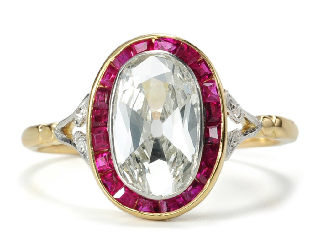 An exceptional diamond with any icy white shimmering hue shares a stage with luscious channel set rubies in a circa 1930 Art Deco ring of 15k yellow gold and platinum. A central old oval cut diamond of an estimated 1.63 carats (H-I color; SI1