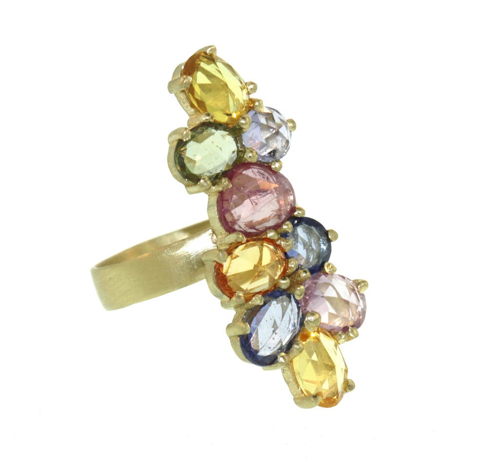 This striking 18k gold ring features nine vibrant rose cut sapphires arranged elegantly along the length of the finger. The stones (7.10ct total) are simply prong set to let them truly shine, creating a long, elegant shape that is especially