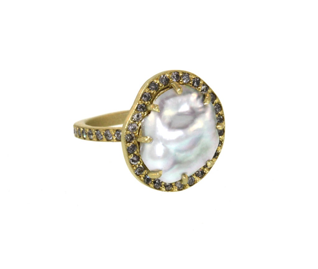 This ring is a beautiful twist on a more traditional solitaire ring. A beautiful keshi pearl sits in a simple 18k yellow gold prong setting surrounded by grey diamonds, on a grey diamond pavé band. The flowing, uneven nature of this particular pearl