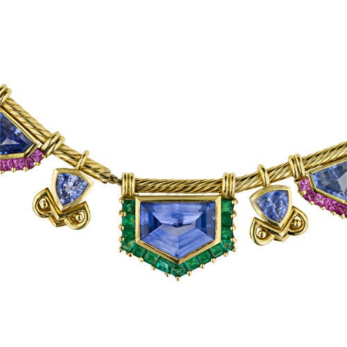 An extraordinary necklace, featuring 55 carats of shield shape, trillion and rectangular blue sapphires, is embellished with pink sapphires and emeralds for a fresh and lively effect. The individual sections are strung on gold chain through sections