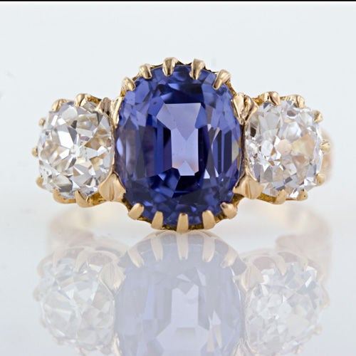 An exceptional and original sapphire and diamond three-stone ring from the late 19th century. A light medium blue sapphire weighing 5.38 carats displaying distinct violet overtones is nestled in a coronet setting and flanked by antique cushion cut