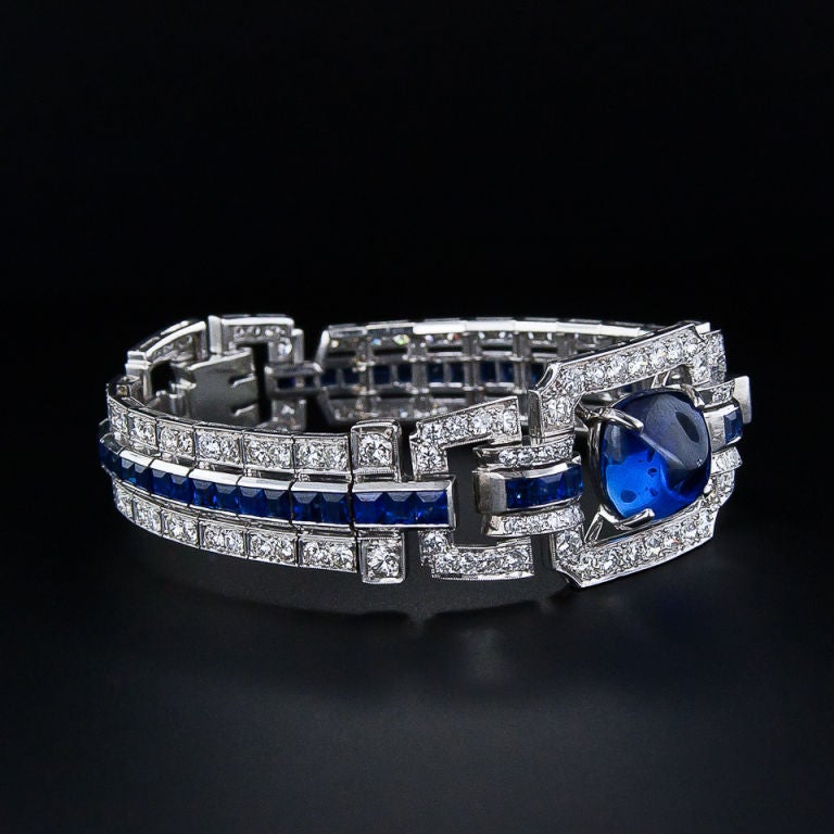 A liquid royal blue 'sugarloaf' cabochon sapphire weighing 13.69 carats floats in the center of this sensational and substantial Art Deco bracelet from the 1930s. The bracelet sections feature a gently graduated line of vivid deep blue sapphires -