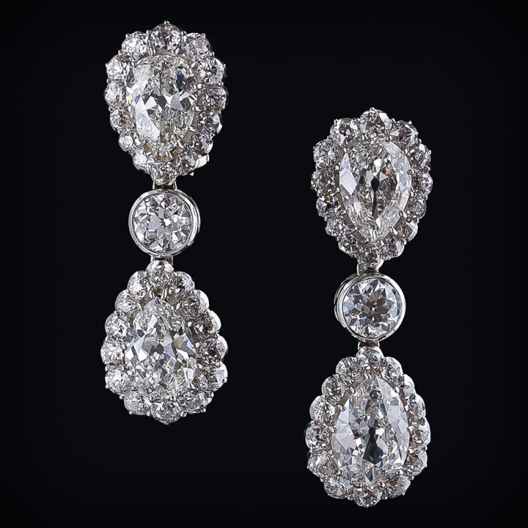 4 antique pear shape diamonds, weighing 8.00 carats total, swathed in a row of European-cut diamonds, are set tip to tip separated by a bezel set .50 carat European-cut diamond in these truly magnificent and regal 1 1/2 inch long drop earrings from