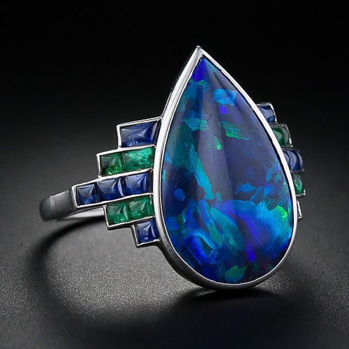 A truly unique and magnificent black opal, sapphire and emerald Art Deco ring from 1920s France. A distinctive, dark pear-shape five carat opal with glowing blue and green flashes is mimicked on the mounting with alternating rows of buff-cut calibre