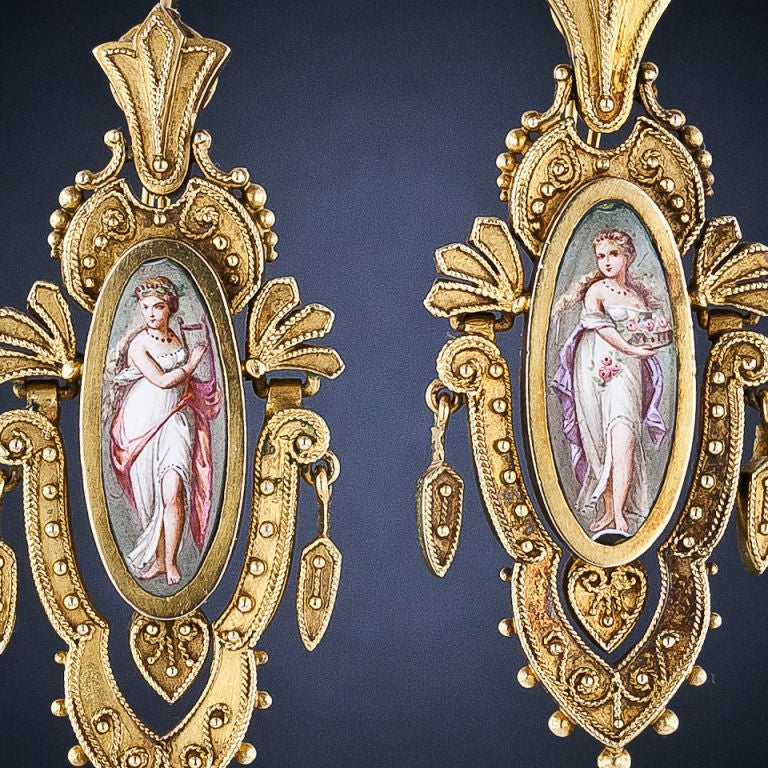 These rare and splendid 1 7/8 inches long Victorian drop earrings magnificently present miniature full length depictions of lovely classical nymphs or muses - one of which arpeggiates dulcet chords on her lyre, the other bearing a basket of fresh