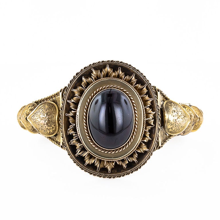 An extraordinarily beautiful and sizable antique bracelet, circa 1875, with a locket compartment on the reverse. This magnificent piece, which measures 1 3/4 inches at its widest point, is designed around a large deep burgundy cabochon garnet.