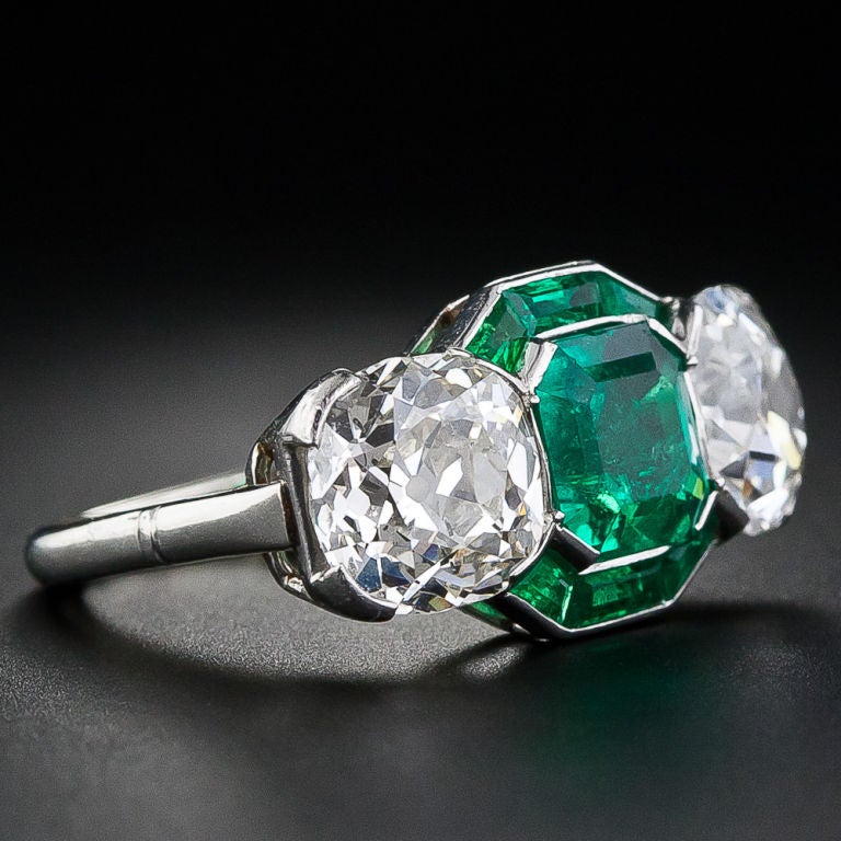 One of the greatest Art Deco Three-Stone rings ever! At arms length, a rich green old mine Colombian emerald looks to be about 4.00 carats (if you include the calibre emeralds embracing it top and bottom!), but it actually weighs 1.50 carats. The