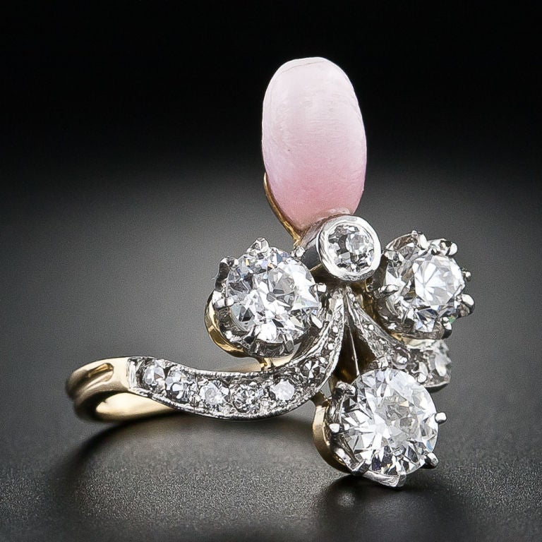 A unique and alluring Victorian ring featuring a natural pink conch pearl and three sizzling white European-cut diamonds, totaling 1.15 carats, arranged in a pattern reminiscent of a fleur d' leis. Hand crafted in platinum over 18ct yellow gold,
