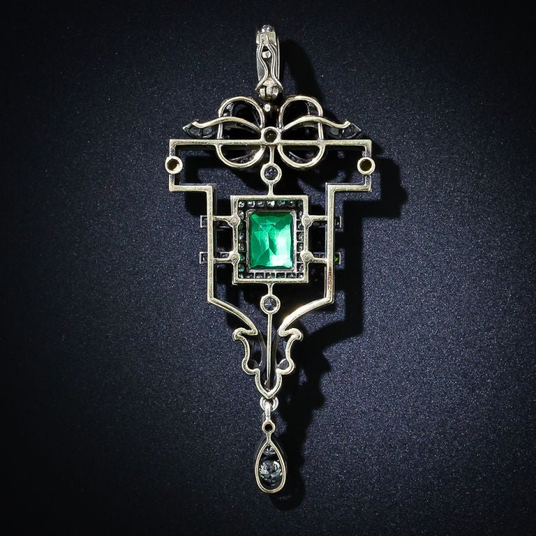 An extra bright, crystal green emerald, weighing 1.25 carats and framed in diamonds, radiates from the center of this magnificent antique pendant, finely hand-crafted in silver over gold. The artfully designed cartouche is outlined with white enamel