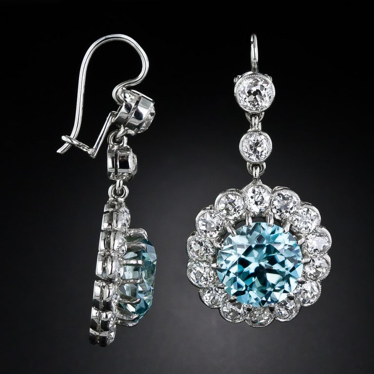 A pair of dazzling and dynamic natural turquoise blue zircons, together weighing 11.50 carats, radiate from within sparkling diamond halos, and dangle from twin-diamond tops, in these dreamy and hypnotic drop earrings, finely crafted in platinum