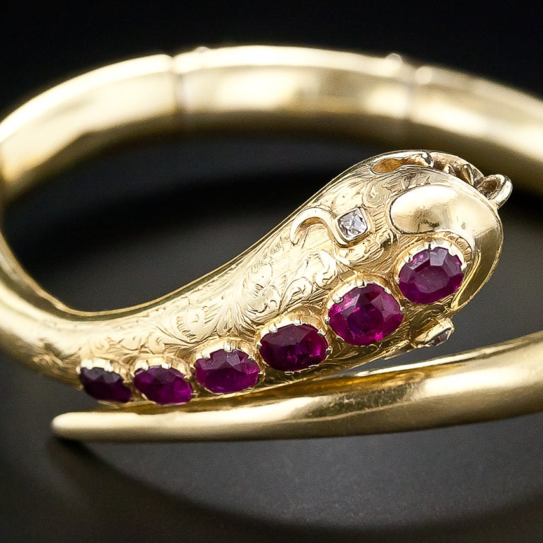 A fierce and toothy diamond-eyed serpent is bedecked with a glistening row of rich red rubies (2.75 carats total) on its exquisitely engraved head and back, in this superb antique hinged bangle bracelet crafted in rich 18 karat yellow gold, circa