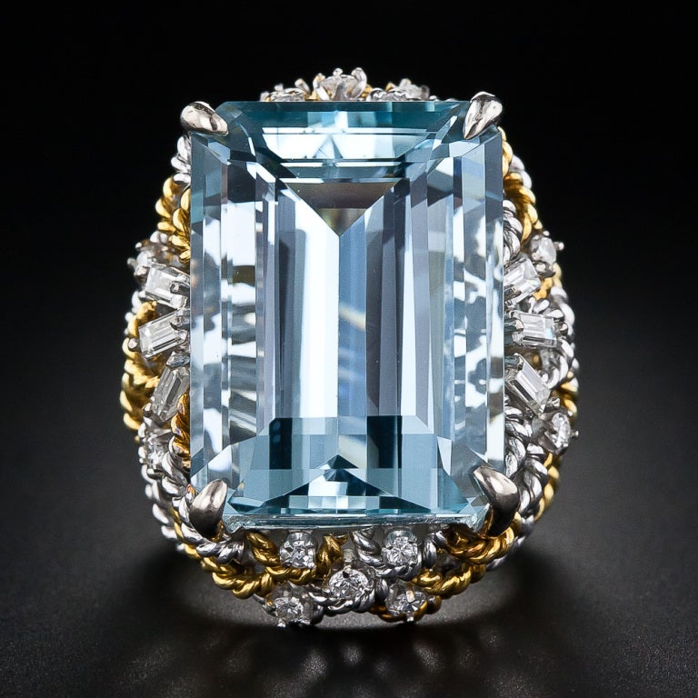 This shining and sizable bauble, starring a 28 carat emerald-cut aquamarine, dates anywhere from the 1960s through the 1980s. The gorgeous gemstone possesses a soothing, deep, pastel-blue color and radiates from atop an artfully designed, two-tone