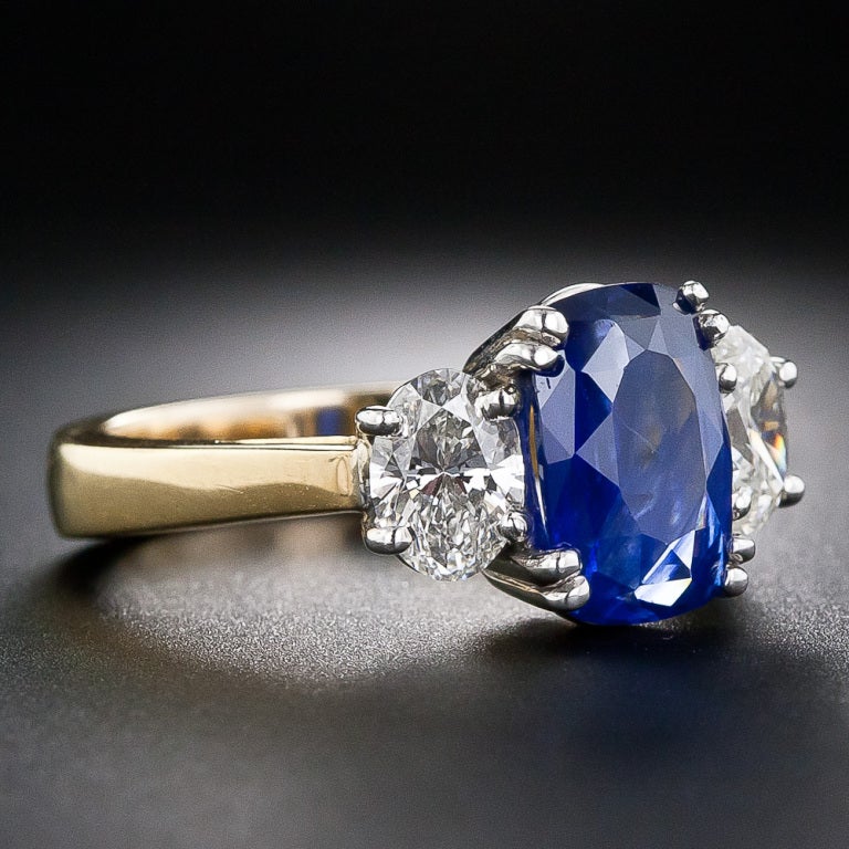 A magnificent oval cushion-cut sapphire, weighing 3.33 carats and displaying a distinctive velvety blue Kashmir-like color, is classically presented between a matched pair of sparkling oval diamonds, together weighing 1.20 carats. The three