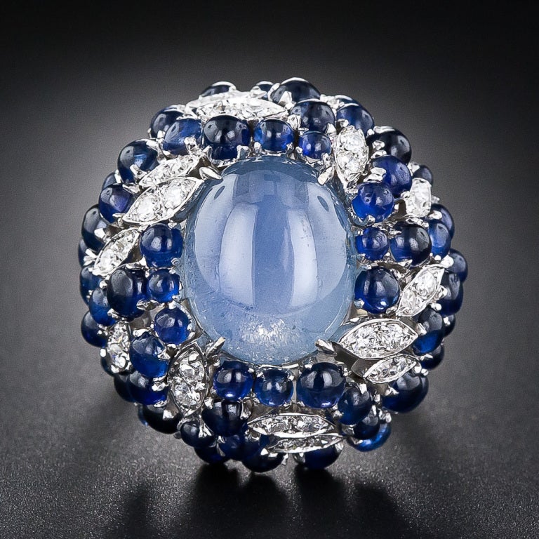 An enchanting 8 carat sky-blue star sapphire, displaying a billowy six-legged star, glows from the center of a big bombe-shape bauble crafted in 18 karat white gold - circa 1960s. The star sapphire is embellished all 'round with diamond-set flames
