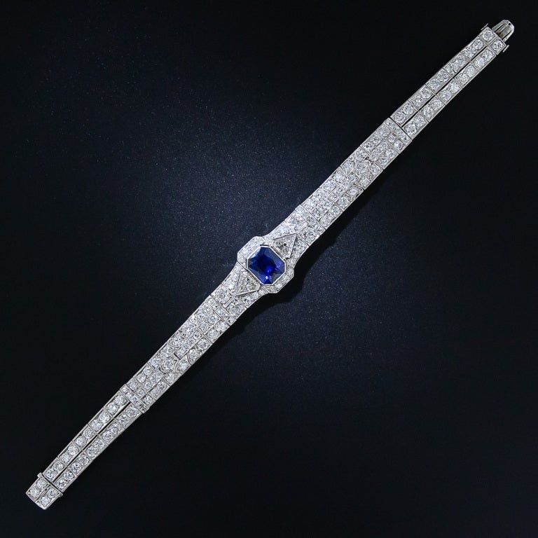 A stunning and exemplary 1930s vintage Art Deco bracelet, crafted in platinum and starring a radiant rich blue faceted emerald-cut sapphire weighing 5.09 carats. The enchanting royal-blue gemstone is flanked on each side by a shimmering kite-shape