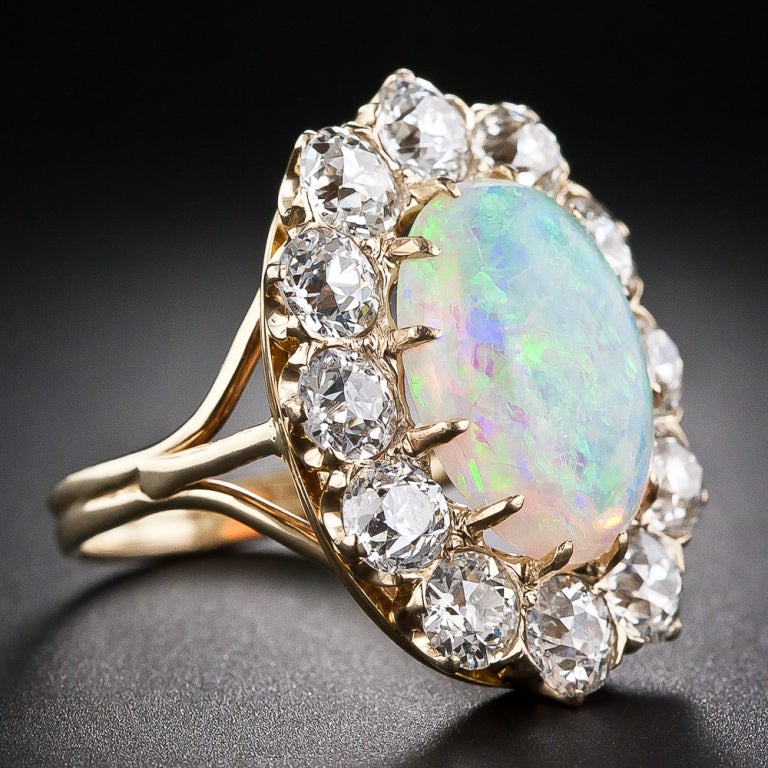 An exquisite antique ring from the Victorian era. A 4.65 carat fine white opal is set ablaze by a fiery diamond border. 4.00 carats of very well matched old mine-cut diamonds embrace the opal which displays shimmering flashes of green and blue.