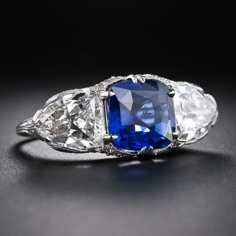 This truly extraordinary ring presents a 4.10 carat cushion-cut sapphire between two exceptionally large bright-white (F-G color) shield-cut diamonds with a total weight of 3.50 carats. The three gemstones sit side by side atop an elaborate gallery