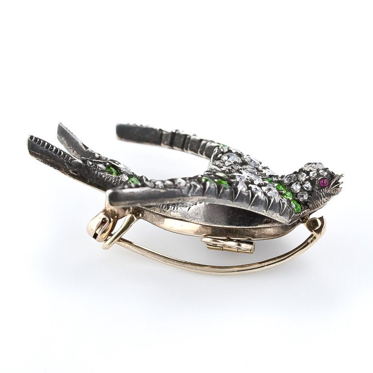A soaring streamlined swallow, crafted in silver over gold, sparkles with bright diamond wings accented with lime-green demantoid garnets in this superb and stunning Victorian jewel - circa 1885. This beautiful bird brooch is outfitted with a