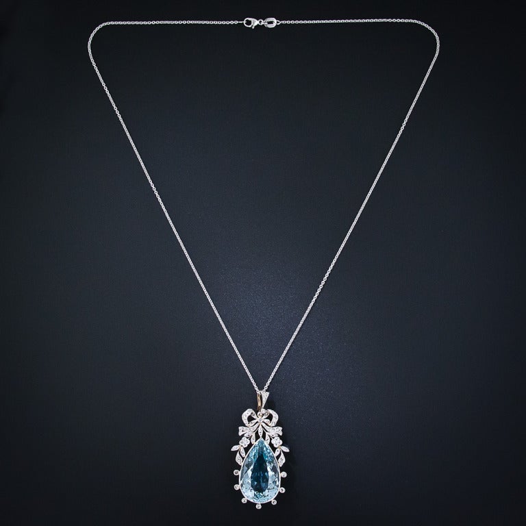 A truly ravishing and romantic aquamarine and diamond pendant necklace from La Belle Époque. A cool, glacier-blue pear-shape aquamarine, measuring 20 carats, is wrapped in glistening diamond ribbons, delicately handcrafted in platinum over 18 karat