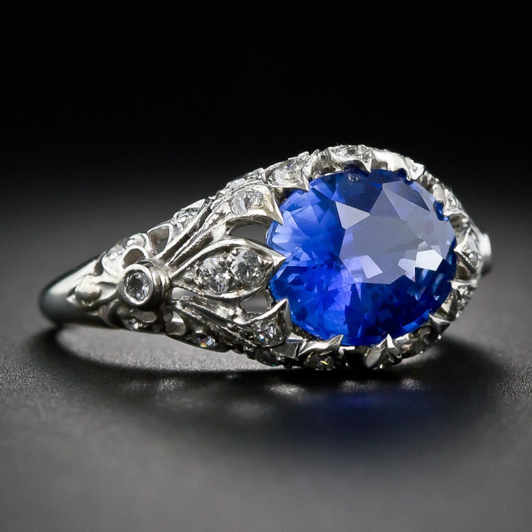 A brilliant 3.23 carat faceted oval, velvety blue sapphire, with just a hint of lavender overtones, radiates from a gorgeous platinum and diamond mounting, handmade during the first or second decade of the twentieth century. The horizontally set