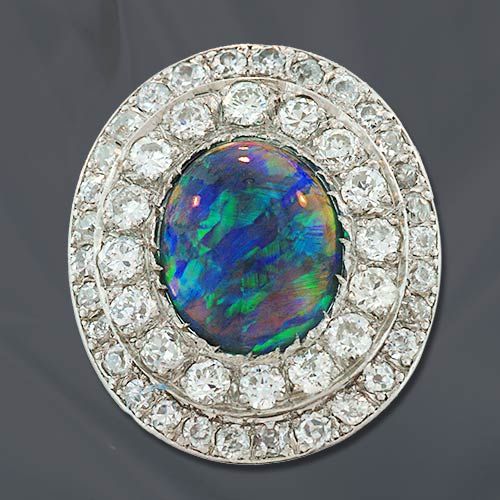 Edwardian platinum ring highlighting a 2.25 carat oval black opal cabochon dancing with blue and green play of color and wrapped in a double border of bead set European cut diamonds.

Inventory No. 30-1-850