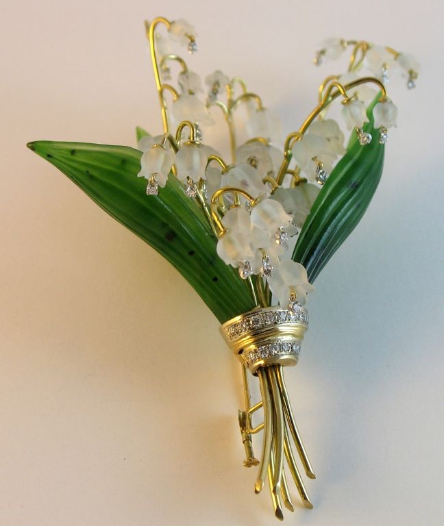 Formed of frosted rock crystal flowerheads, each centering a small round diamonds, the leaves of carved nephrite, the stems bound by a double rope of round diamonds, mounted in gold.<br />
<br />
<br />
<br />
<br />
For similar please note