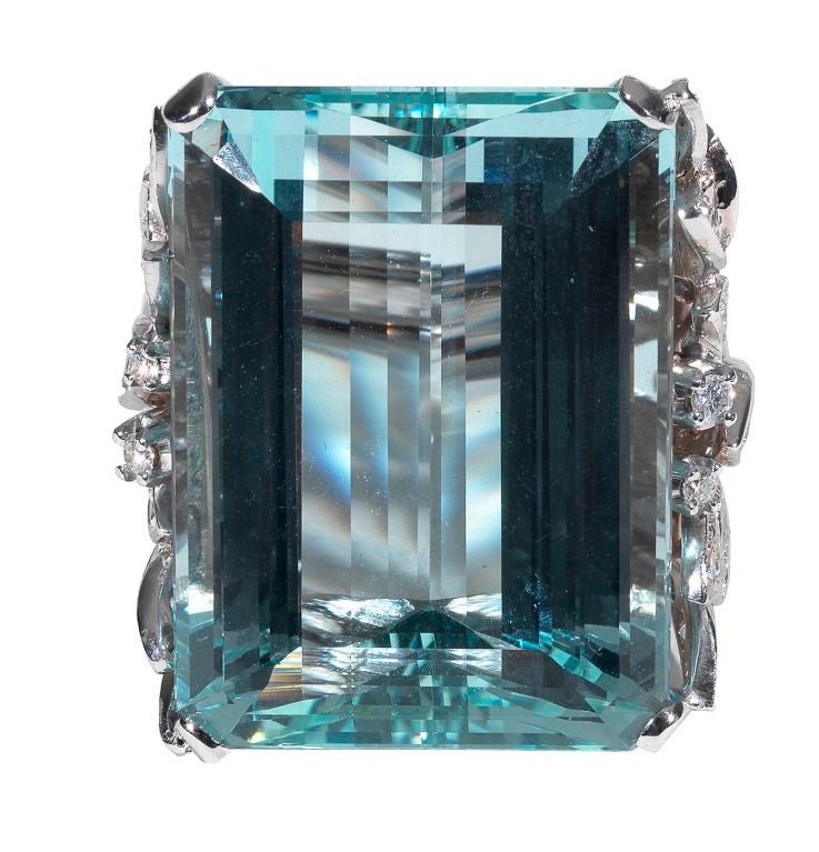 Claw-set with a step-cut aquamarine weighing 51.86 carats, within a brilliant-cut diamond shoulder weighing 1.12 carats, mounted in white gold.

Weight: 26.3 gr

PLEASE NOTE: OUR PRICE IS FULLY INCLUSIVE OF SHIPPING, IMPORTATION TAXES & DUTIES