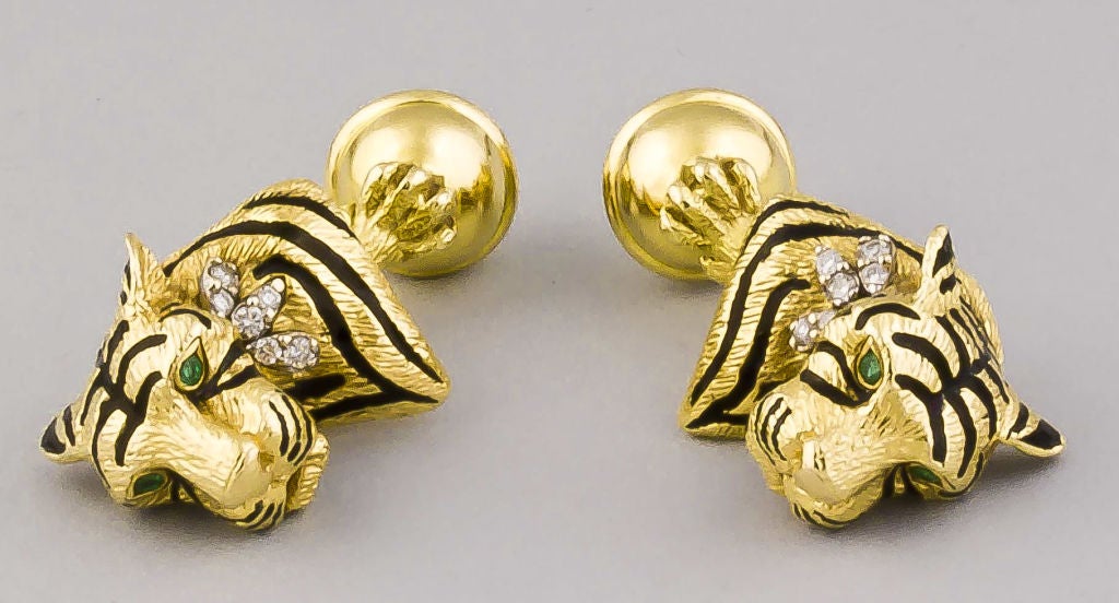 Rare and unusual 18K gold, enamel and diamond tiger bust cufflinks, by Tiffany & Co.. They feature a tiger bust with black enamel stripes, emerald eyes and diamond accents. The other end features a gold sphere held by a tiger's paw. Discontinued,