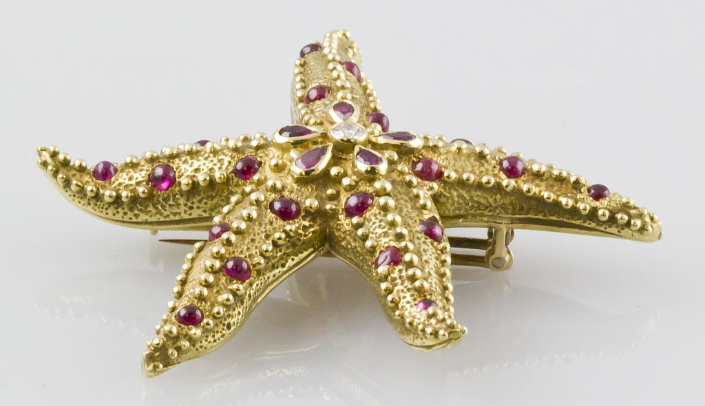 Rare and unusual 18K gold, diamond and ruby brooch by Tiffany & Co. Schlumberger, circa 1960s. It features a bezel set diamond in the middle, surrounded by 5 pear shaped rubies and set throughout the starfish rays are cabochon rubies.
Hallmarks: