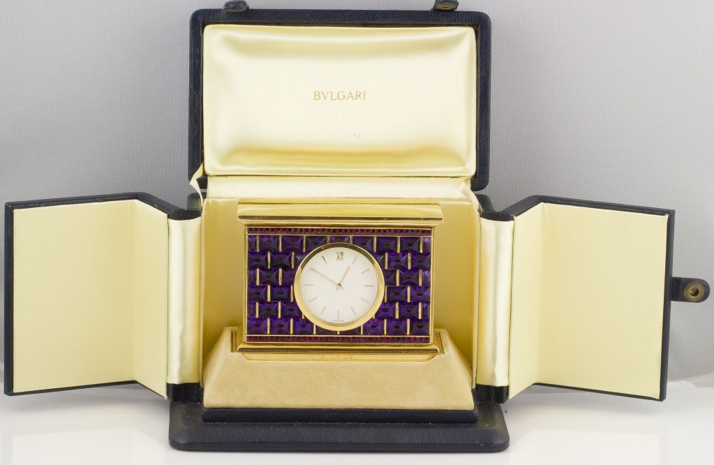 Rare and unusual 18k yellow gold, amethyst and ruby mantle clock by Bulgari. It features a column design and the front is reminiscent of a brick-like facade. Quartz movement with Roman and baton numeral dial. 
Hallmarks: Bulgari, French 18K gold