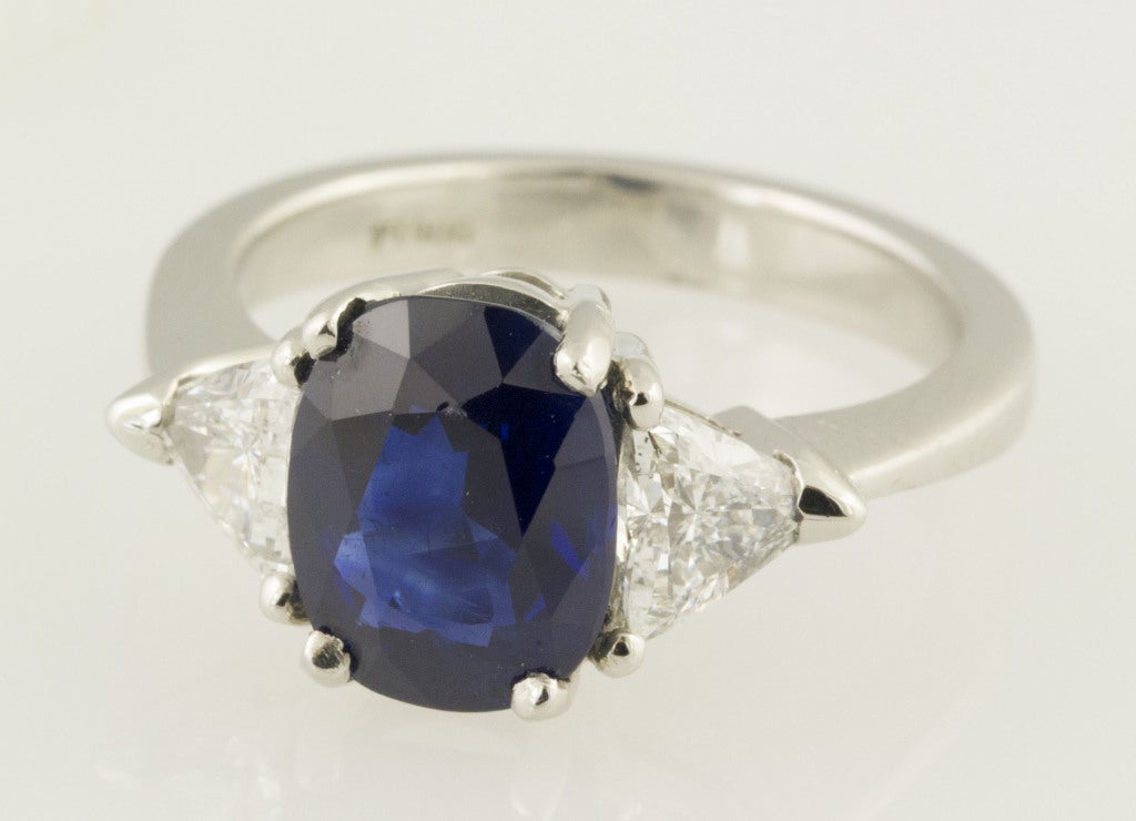 Timeless sapphire and diamond three stone platinum ring. It features a very high grade oval faceted 3.58ct natural sapphire flanked by two high grade triangular shaped diamonds, measuring approx. 0.85-1.00cts total weight. Comes with AGT certificate