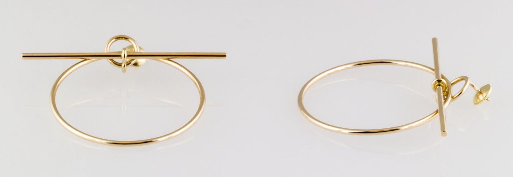 Impressive 18K gold hoop earrings by Hermes. They feature a round hoop with a bar across the top, and are worn like studs.        
Hallmarks: Hermes, reference numbers, AU750.