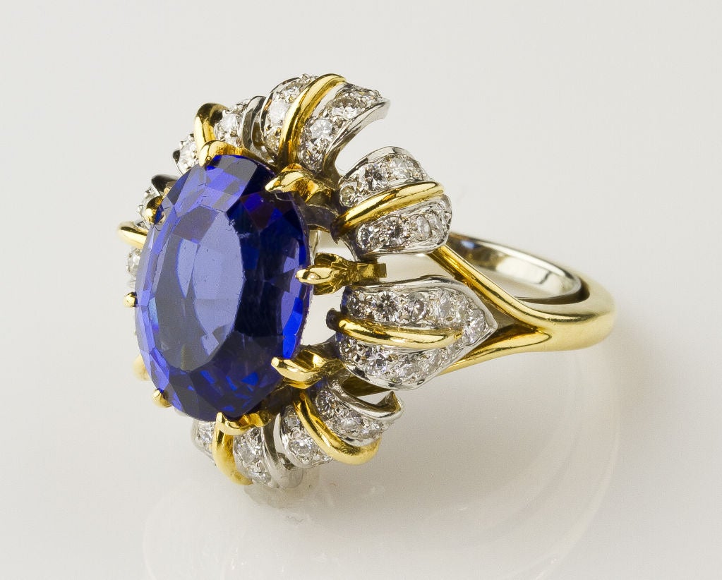 Stunning oval tanzanite ring set in platinum and 18K gold surrounded by diamonds in a flower-like setting, by Tiffany & Co. Schlumberger.  The tanzanite is oval faceted cut, 9.34 carats in weight, violetish blue hue, medium dark tone.  It is